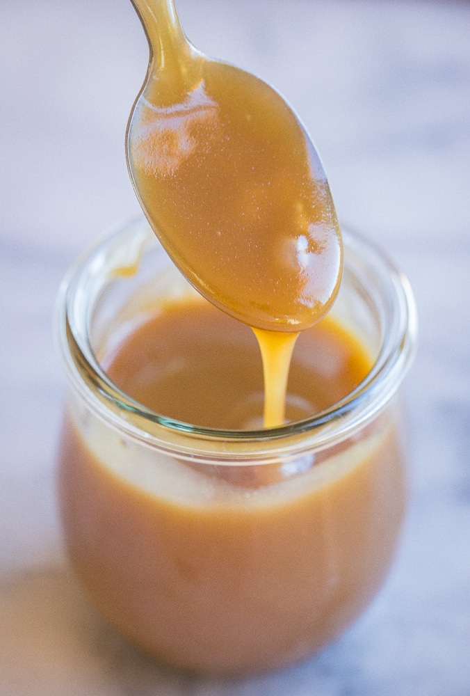 a spoon being dipped into a jar of salted caramel sauce