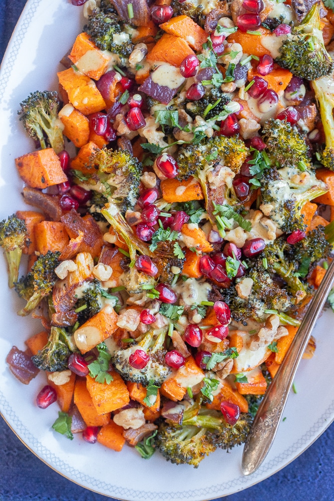 serving platter full of roasted sweet potato and broccoli with curry tahini sauce and pomegranate seeds.