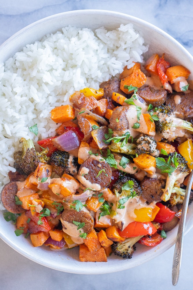 big bowl of vegetarian sheet pan dinner with sausage and vegetables with a drizzle of bbq tahini sauce