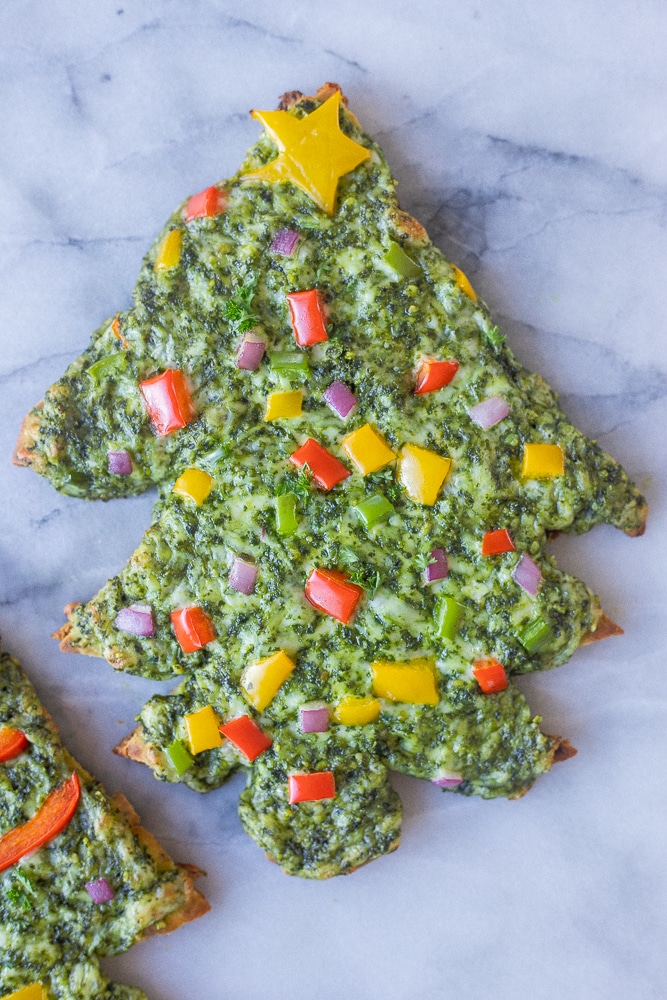 close up of a cheesy christmas tree naan pesto pizza topped with colorful veggies
