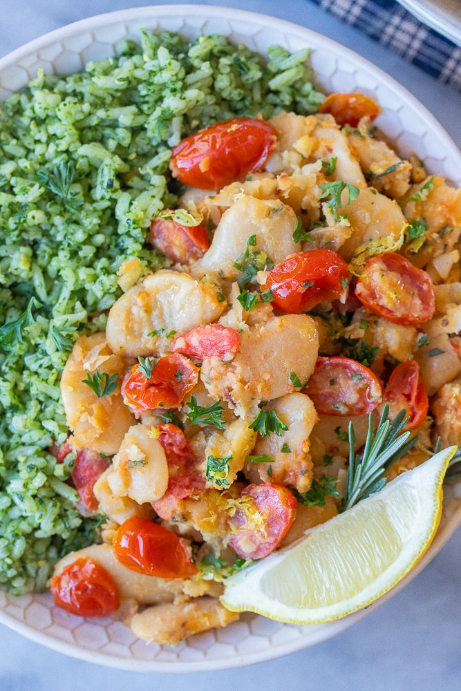 close up of a bowl of butter beans seasoned with herbs served over pesto rice