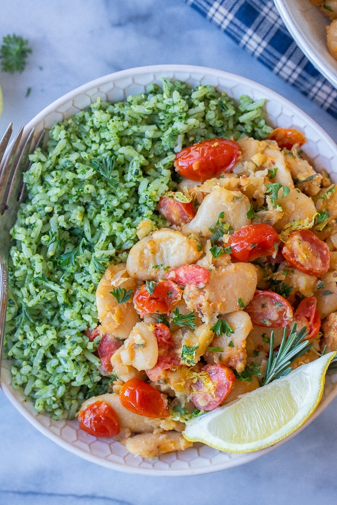 a bowl of tomato herb butter beans with green pesto rice with a lemon wedge
