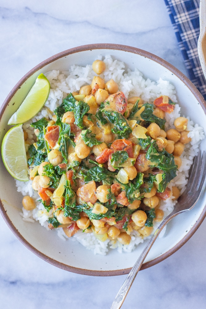 coconut curry with chickpeas and kale in a bowl with rice and fresh limes
