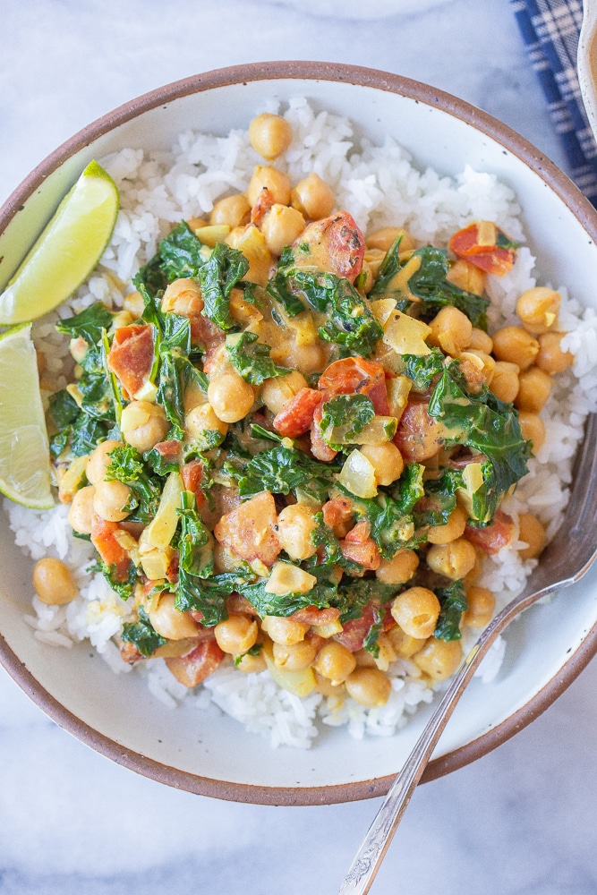 close up of a bowl of quick and easy chickpea curry with kale over rice with a side of lime wedges