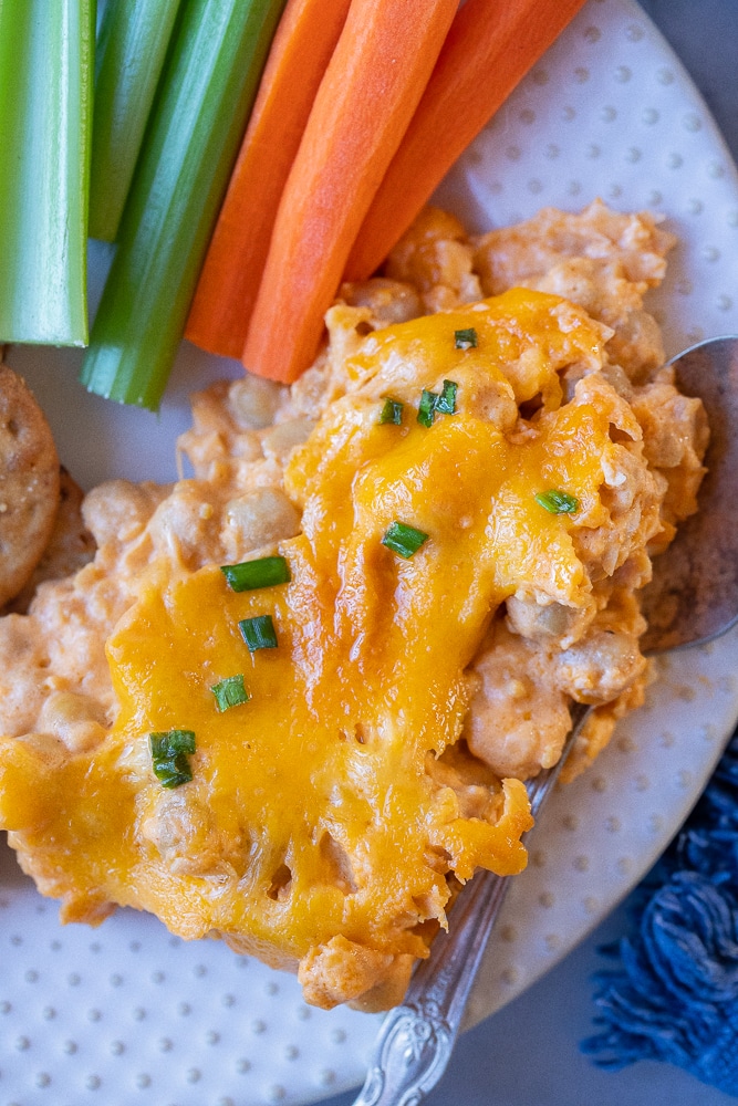 close up of a scoop of buffalo chickpea dip on a plate with carrots and celery