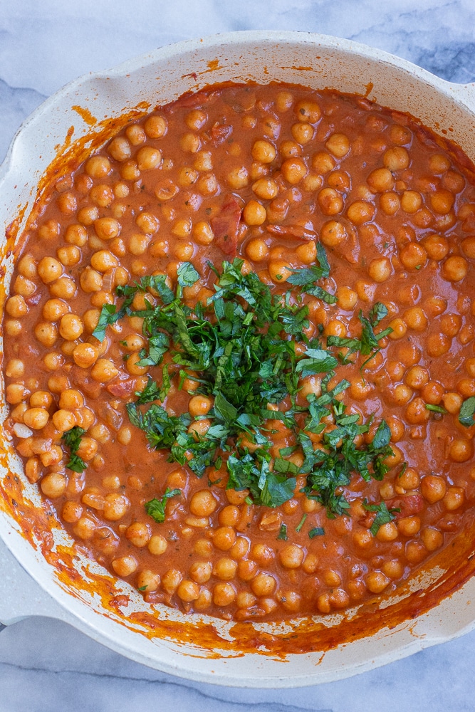 smoky and creamy chickpeas in a pan topped with fresh herbs