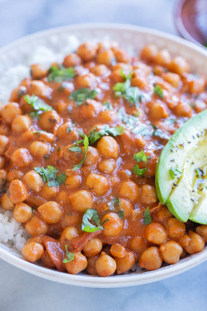 close up of butter chickpeas in a bowl with rice and fresh herbs