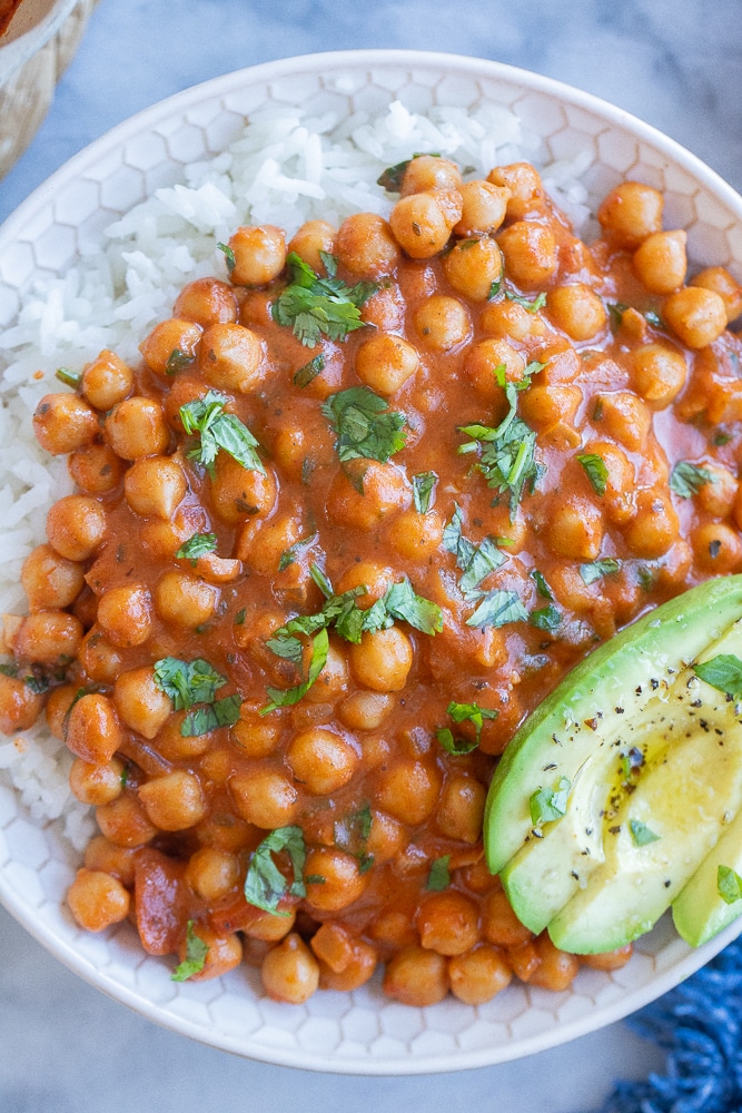 close up of saucy chickpeas in a bowl with rice and avocado