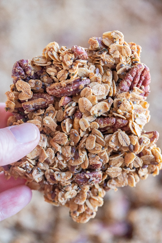 a hand holding a large piece of large clustery granola