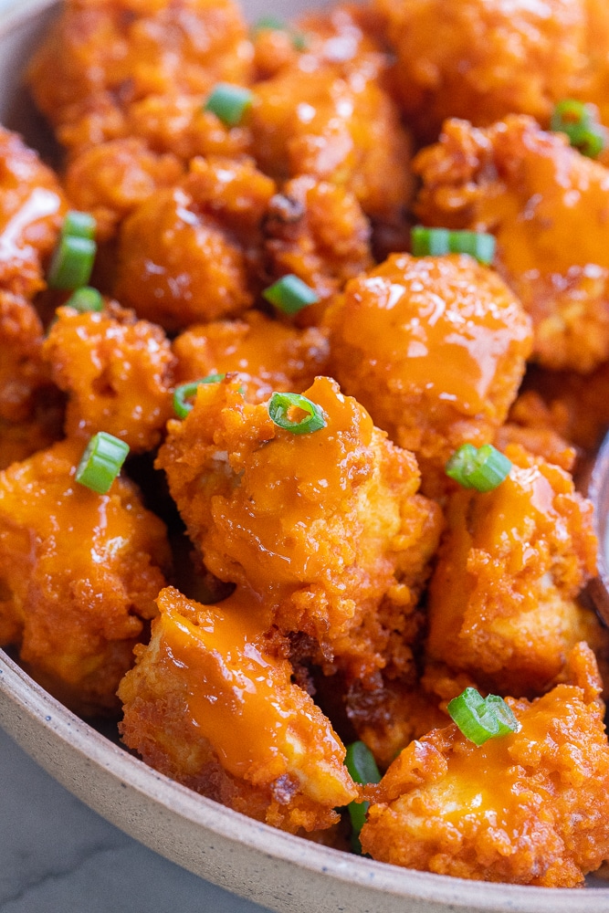 close up of a bowl of vegan buffalo tofu wings with green onion