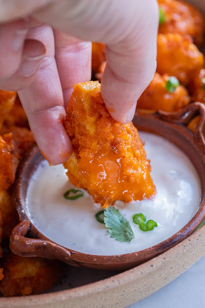 a hand dipping a buffalo tofu wing into some ranch dressing