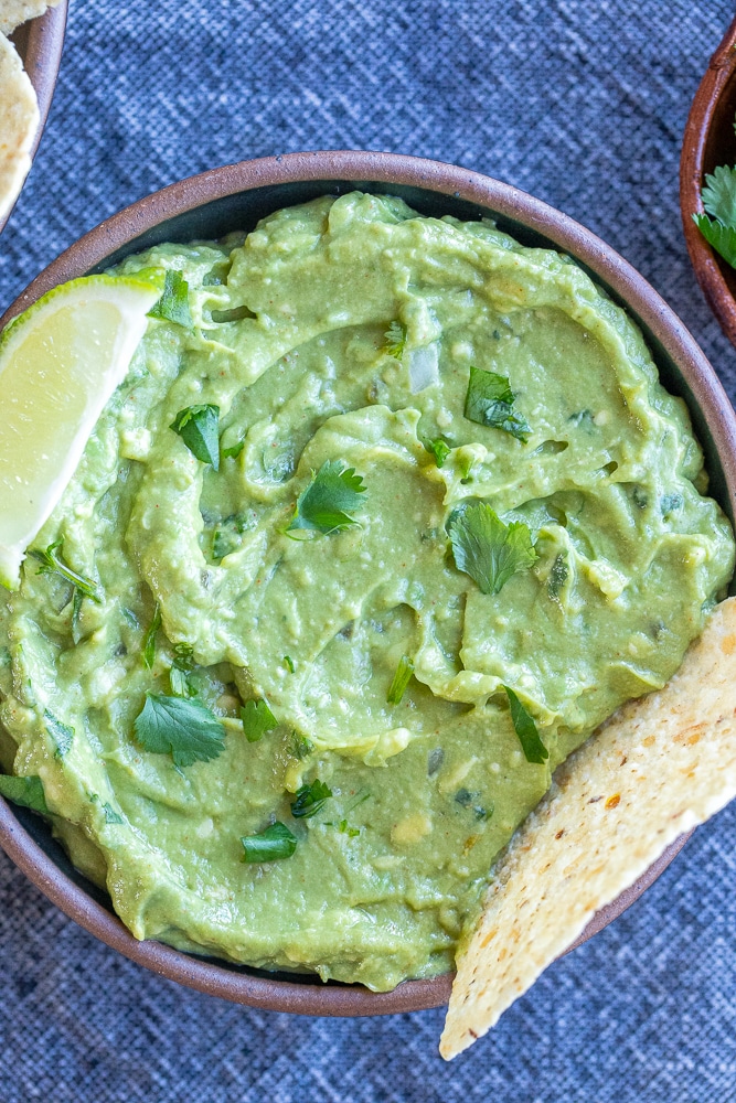 bowl of the best guacamole with a lime wedge and tortilla chip