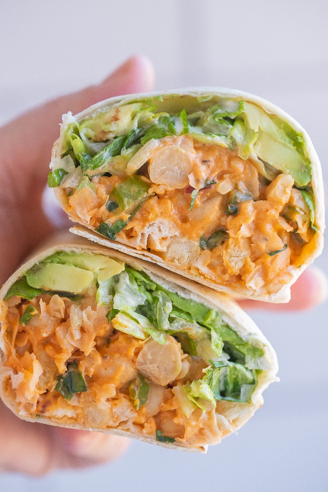 buffalo chickpea wrap that has been cut in half being held by a hand
