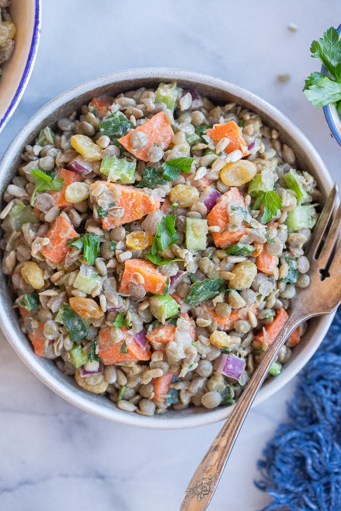 bowl of lentil and roasted carrot salad with a fork and blue napkin