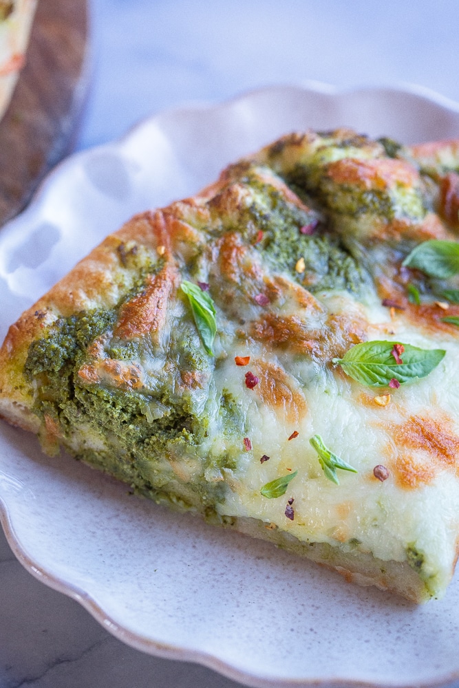 close up of a slice of the best vegetarian pesto pizza on a plate