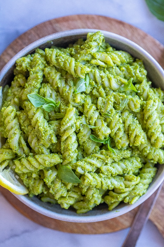 close up of a green goddess pasta with parmesan in a bowl with basil and lemon wedges