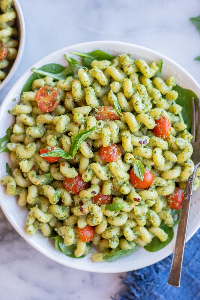 creamy avocado pesto pasta in a serving bowl with cherry tomatoes and basil