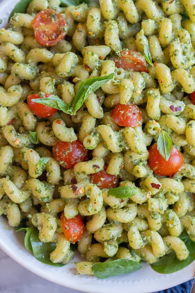 Close up of vegan avocado pesto pasta with cherry tomatoes and fresh basil