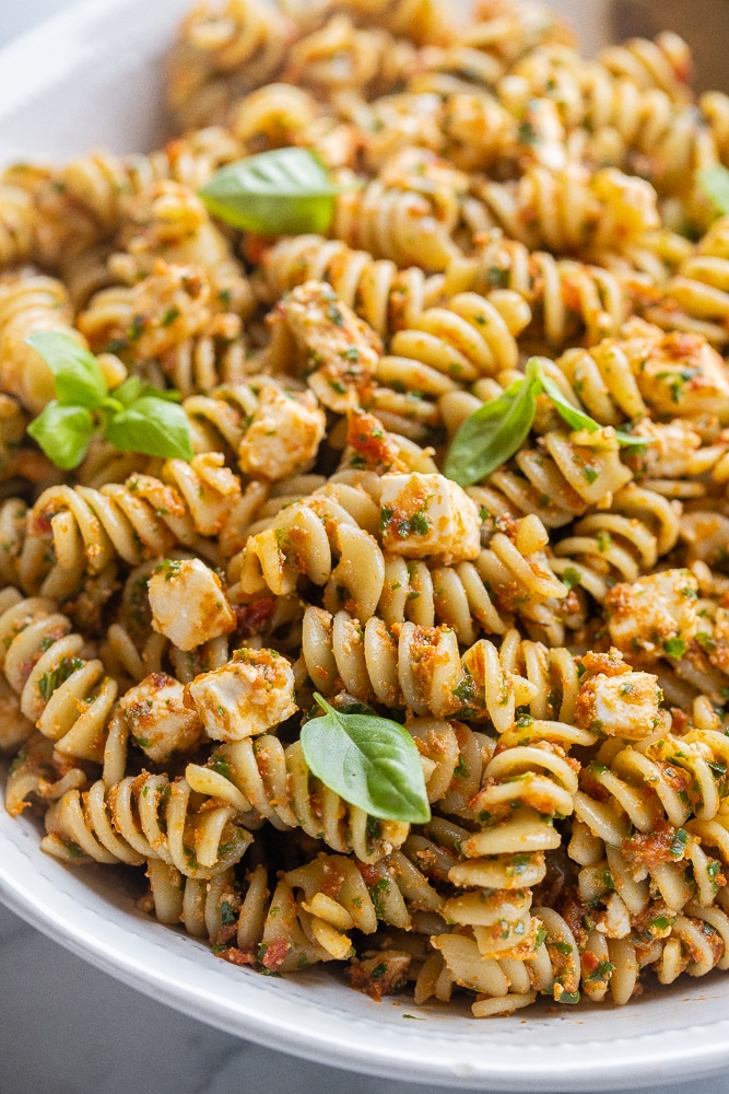 close up shot of a bowl of kale and sun-dried tomato pasta with fresh basil
