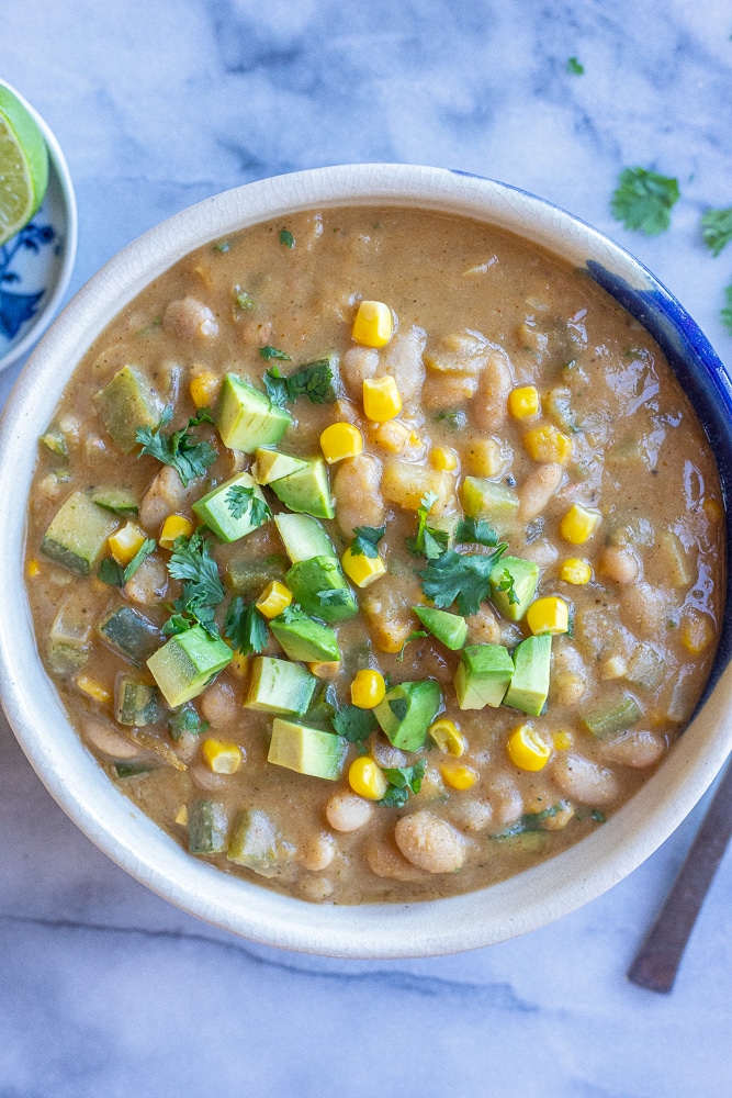 big bowl of vegan zucchini corn and white bean chili topped with diced avocado and corn