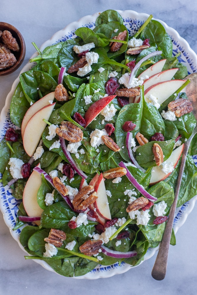 platter filled with this easy spinach salad that is topped with apples, onion, cranberries and pecans