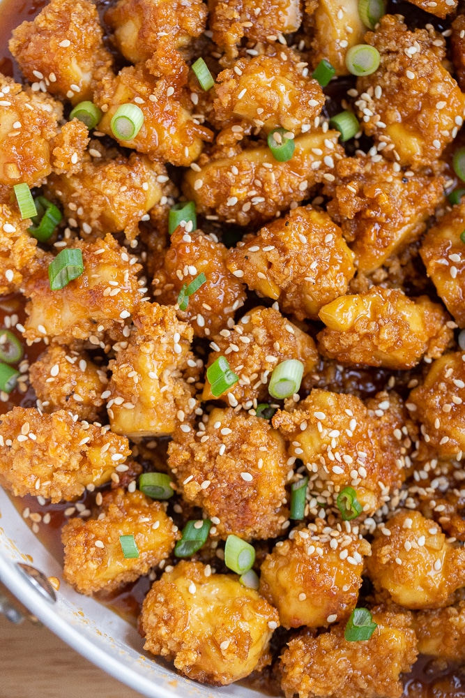 close up of honey garlic tofu in a pan with green onion and toasted sesame seeds