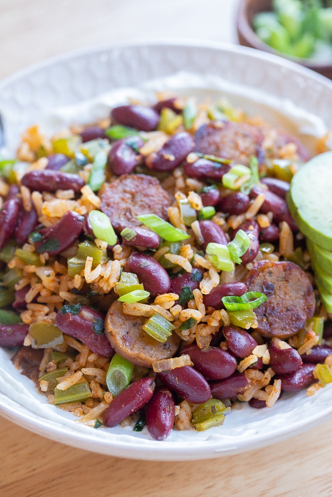 close up of a bowl of vegetarian red beans and rice topped with sliced green onion and avocado