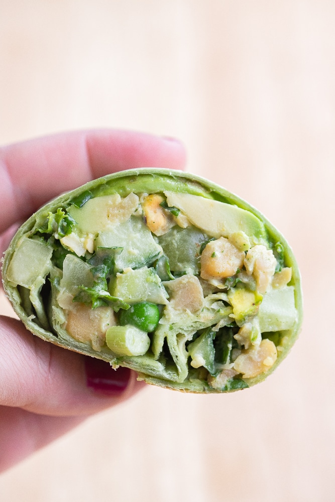close up of a vegan green goddess chickpea wrap cut in half held by a hand