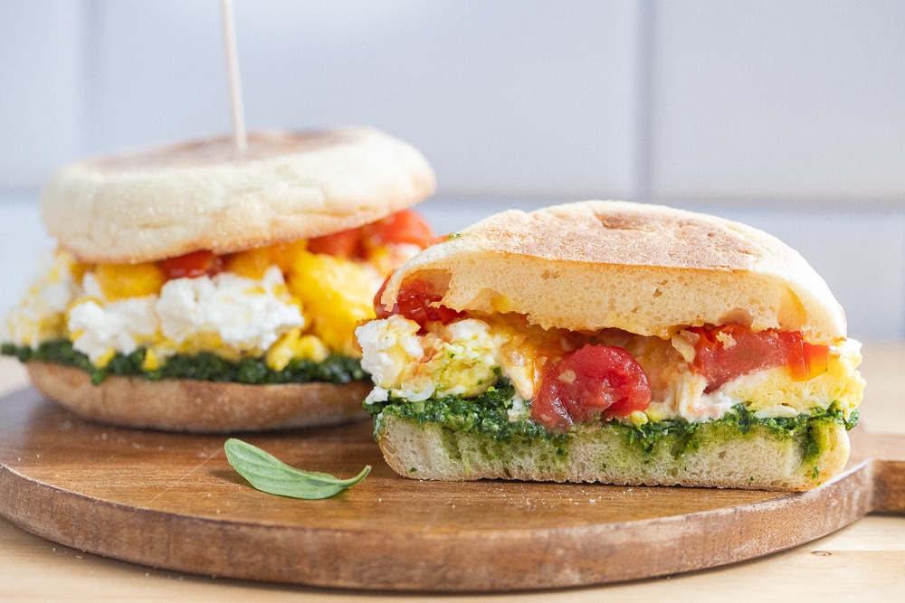 tomato goat cheese breakfast sandwich with kale pesto cut in half on a cutting board