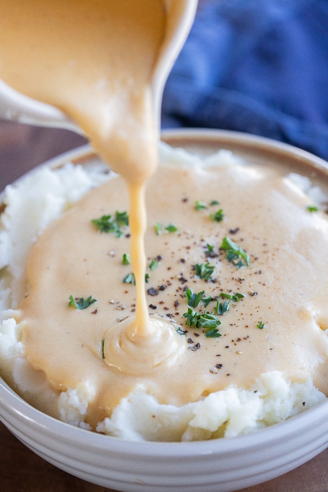 gravy being poured onto a bowl of mashed potatoes