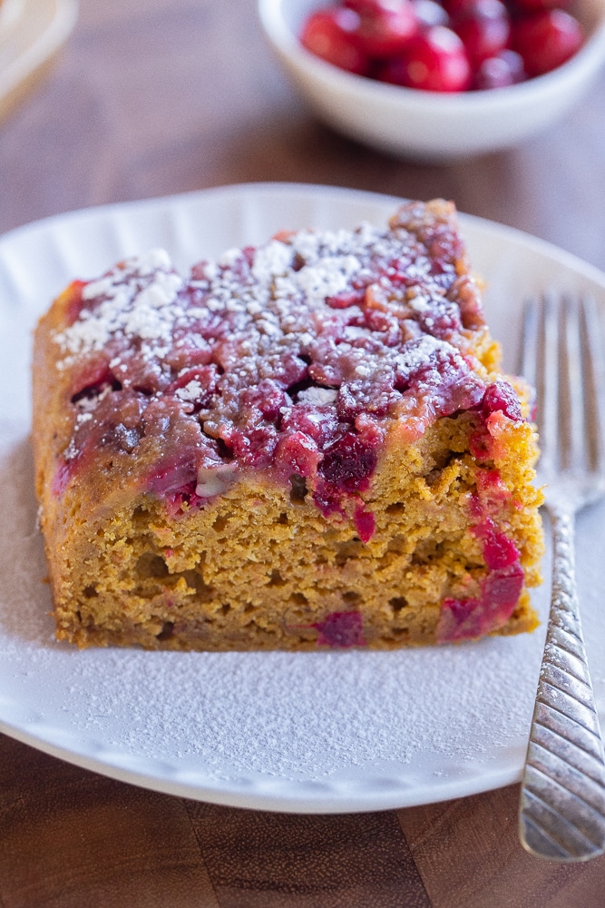 close up of a slice of cranberry upside down pumpkin cake topped with powdered sugar