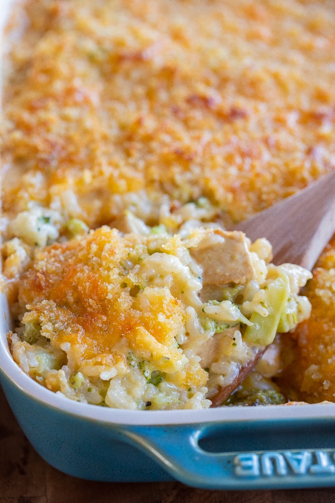 close up of a wooden spoon in the casserole dish holding the broccoli rice casserole
