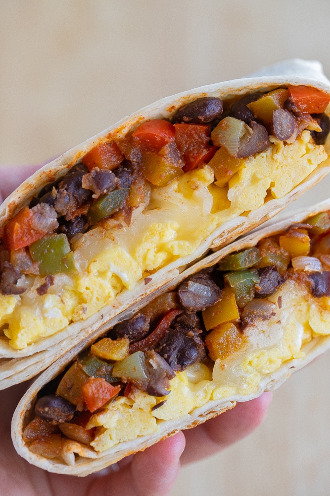 close up of a hand holding a fajita breakfast wrap that has been cut in half
