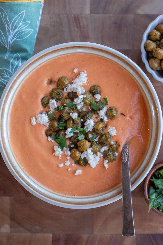 creamy roasted tomato feta soup in a bowl topped with pesto chickpeas and feta crumbles