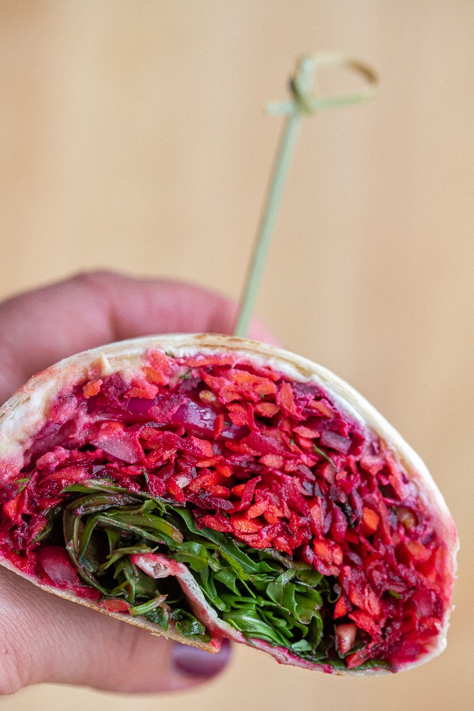 a hand holding a carrot beet wrap that has been sliced in half