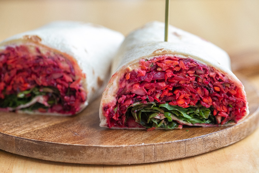 close up of a carrot and beet hummus wrap on a cutting board