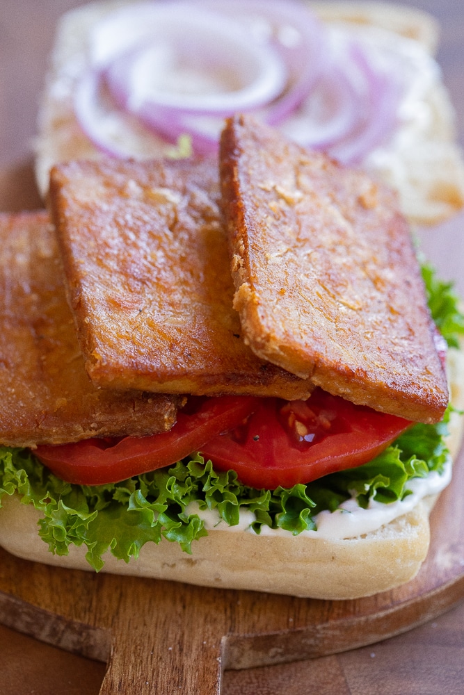 close up slices of tofu bacon on top of a sandwich