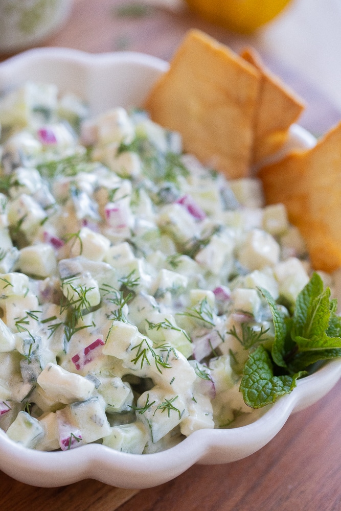 close up of a bowl of cucumber salad with yogurt and fresh herbs