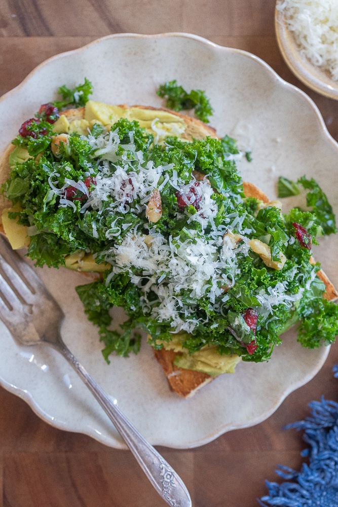 serving plate with a slice of avocado toast topped with kale salad