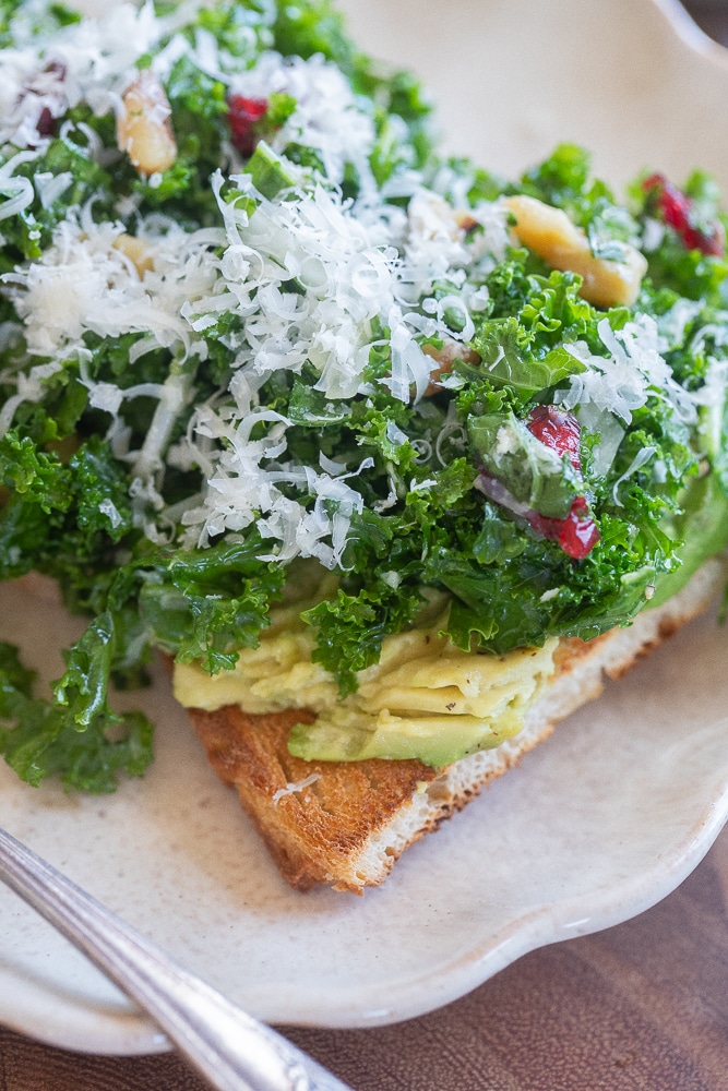 Close up of a slice of toast topped with avocado and kale salad