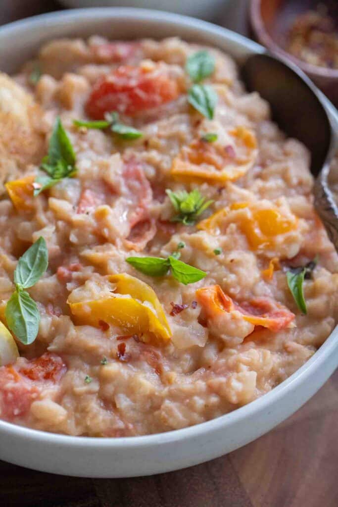 Close up of a bowl of mashed great northern beans with basil and tomatoes