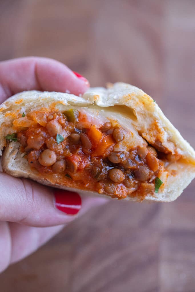 A hand holding a meaty lentil sub that has been cut in half