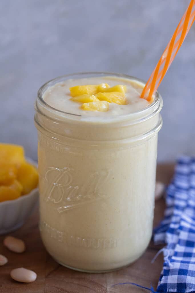 white bean mango smoothie in a cup with a straw