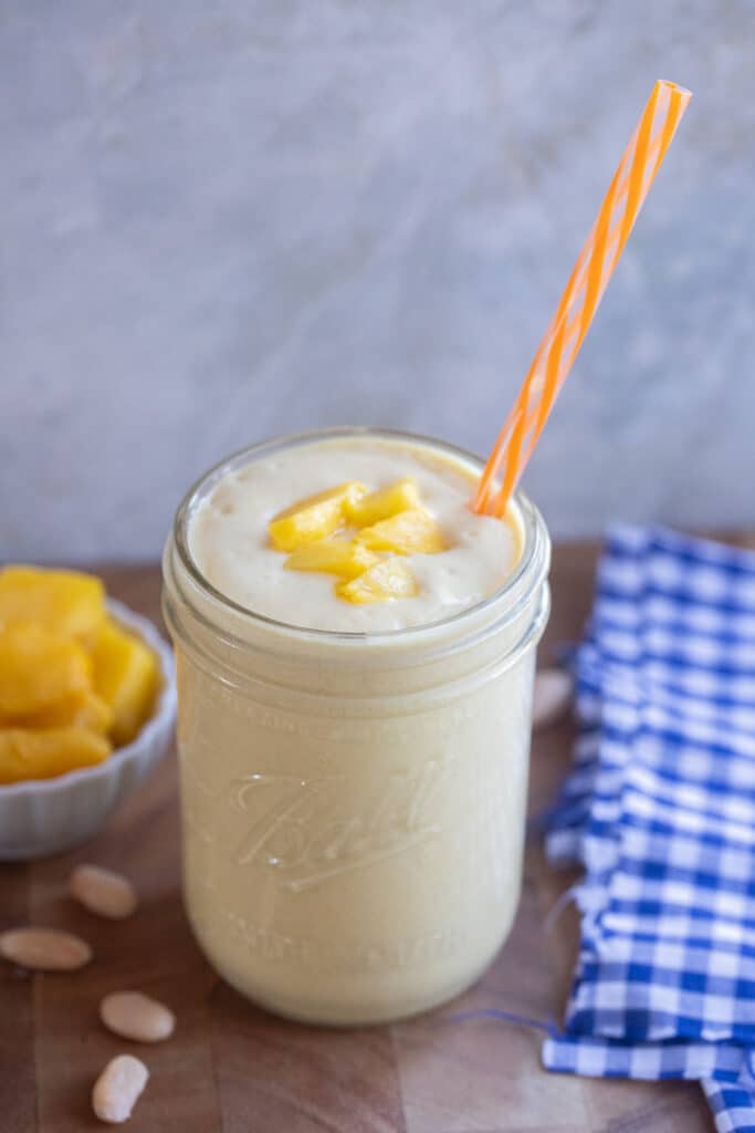 white bean smoothie with mango in a glass jar with a straw