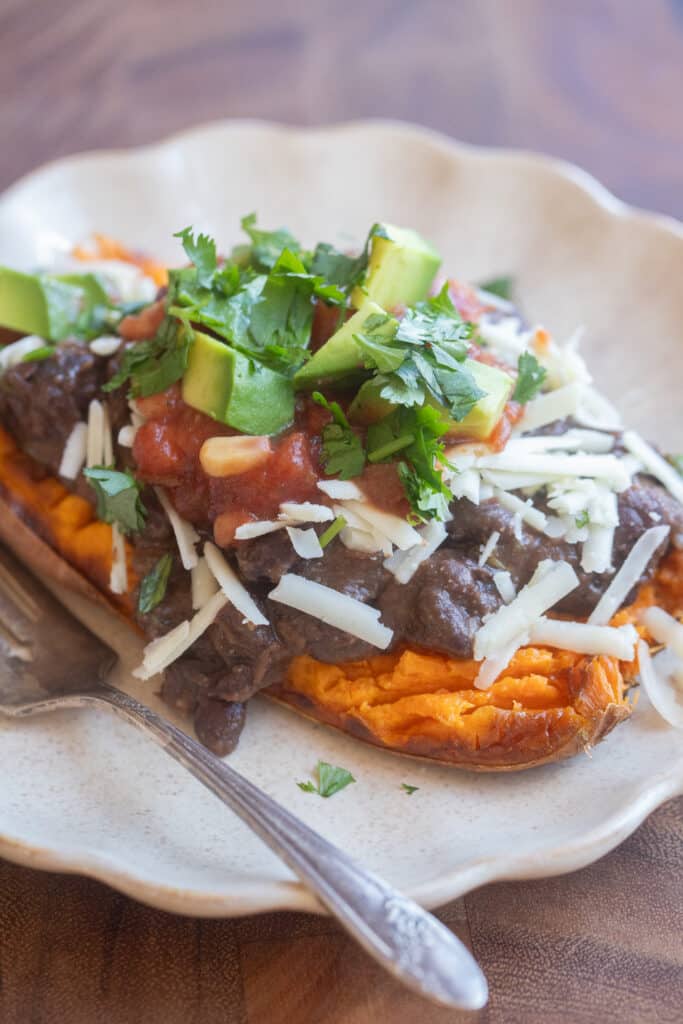 close up of a roasted sweet potato half topped with black beans and cheese