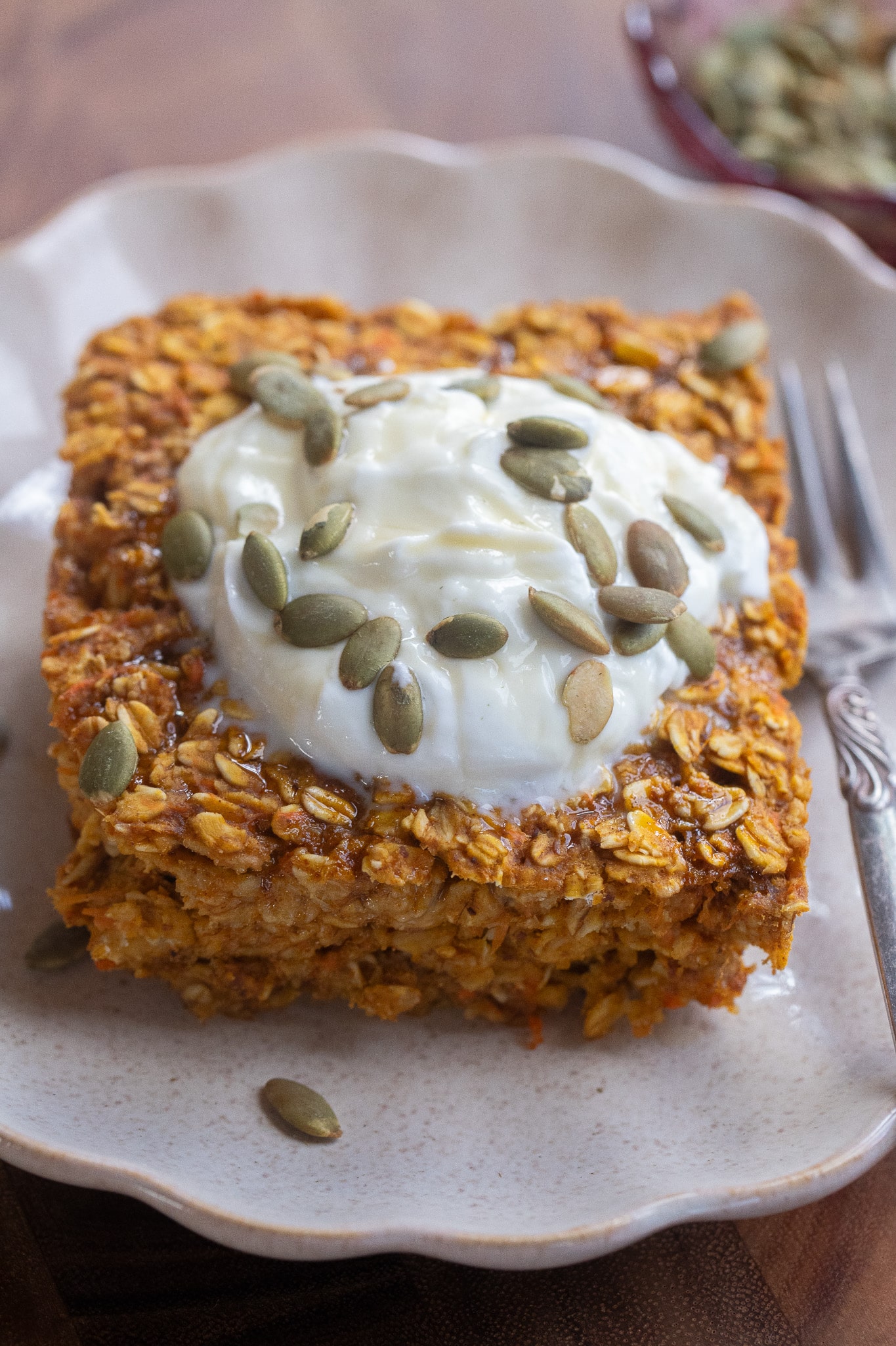 close up of a slice of pumpkin ginger turmeric baked oatmeal on a plate topped with yogurt and pumpkin seeds.